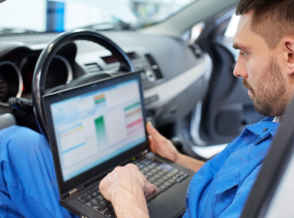 Mechanic in blue overalls in the drivers seat of a vehicle with a computer on his lap looking over some vehicle data - Car Diagnostics Peckham